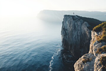 A solitary lighthouse stands on majestic cliffs towering over the misty sea, creating a captivating...