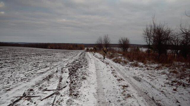 Soldiers in full gear walk across a field in winter. Ukrainian soldiers patrol the area. Soldiers with machine guns go to the shooting range.