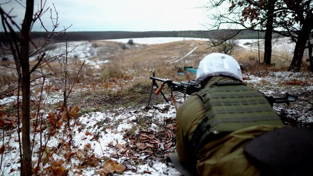 A machine gunner fires a machine gun on a military field. Many spent machine gun cartridges are on the ground. A machine gunner lies on the cold ground with a firearm. Military training
