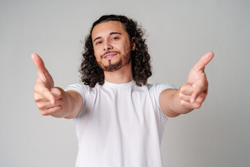 A smiling young man with curly hair playfully pointing directly at the viewer in a light-colored...
