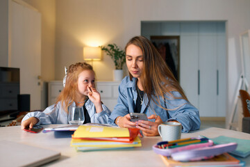 A schoolgirl sits at home with her mother and does her homework