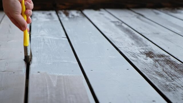 Close-up of a brush painting a wood floor in brown color. Wood plank impregnation. Oil coating of a board. Second layer of oiling. Manual construction work in a gazebo. Natural building materials. 4K