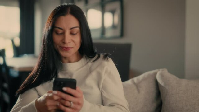  Woman holding smartphone sitting on couch at home Woman with cell phone surfing internet using social media apps. Shopping online Internet news cellphone. Talking on the phone