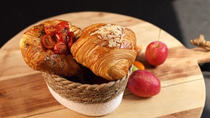 Croissants with tomatoes, cheese inside basket, apples placed nearby on wooden surface, autumn...