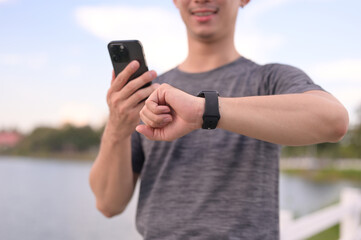 Athletic man holding mobile phone and checking heart rate on smartwatch