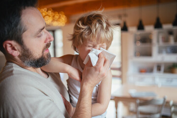 Sick boy with cold at home. Father helping little son to blow his nose.