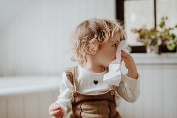 Sick girl with cold at home, blowing her nose.
