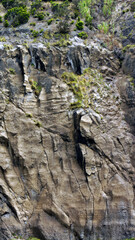 The photo shows volcanic rocks against which white ocean waves are crashing. Sunny weather and blue sky add to the holiday atmosphere. The rocks are wet and shimmer with sandy and gray shades.