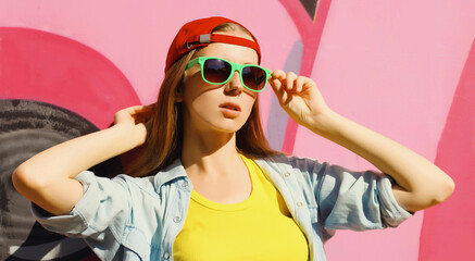 Stylish young girl in baseball cap, glasses, modern teenager girl posing against the graffiti wall