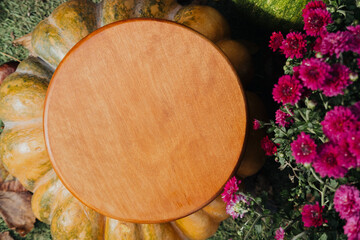 Wooden table atop a large squash surrounded by colorful flowers in sunlight