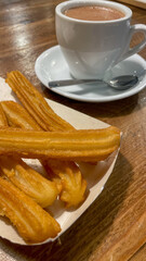 A plate of golden churros with a steaming cup of hot chocolate on a wooden table, perfect for Spanish holiday traditions
