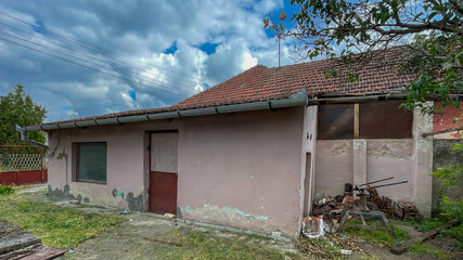 Weathered rural house with peeling paint under a cloudy sky highlights rural decay and renovation challenges