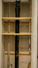 A view of exposed plumbing pipes and shelves in a utility cabinet, highlighting home renovation and maintenance challenges