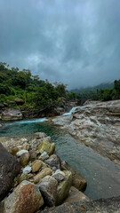A serene mountain river flows through lush greenery and rocky terrain under a cloudy sky, perfect for nature relaxation themes