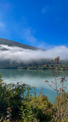 Fototapeta premium A serene mountain lake shrouded in mist under a clear blue sky, perfect for promoting tranquility and nature escapes