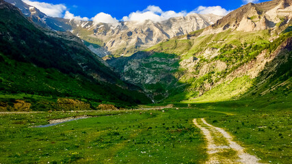 Scenic mountain valley landscape with a dirt path under a clear blue sky, ideal for nature tourism and adventure holidays