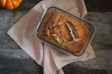 Top view of a freshly baked beautiful loaf of sourdough bread in on a weathered vintage wooden table with a small pumpkin on the side