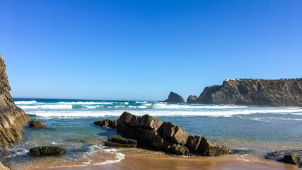 Scenic coastal landscape with rugged cliffs and crashing waves under a clear blue sky, ideal for summer vacation concepts