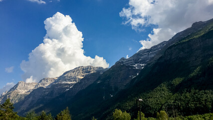 Fototapeta premium Majestic mountain landscape with lush greenery and dramatic clouds under a bright blue sky, perfect for Earth Day appreciation