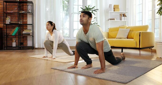 Indian Asian young couple joyfully practicing yoga together in their lavish home, executing Ek Pad Prasarita Padasana, or One-Legged Wide-Legged Forward Bend pose