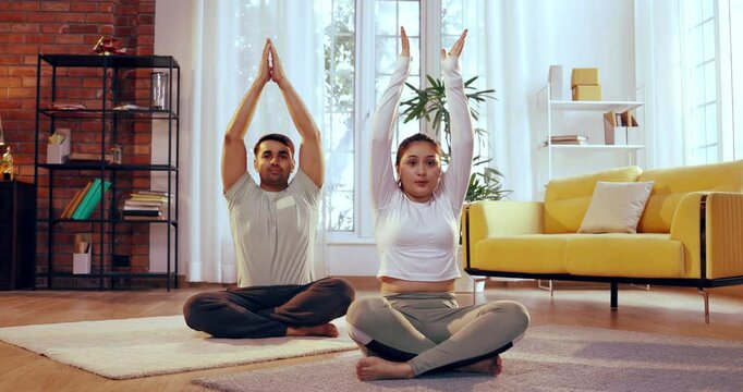Indian Asian young couple learning yoga together in their lavish home, performing Parvatasana or seated mountain pose, focusing on alignment, posture, and inner balance in a peaceful environment