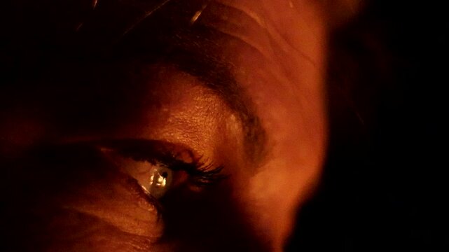 Closeup of a Female eye reflecting the warm, glowing embers created by an outdoor fireplace at night, intimate atmosphere