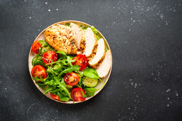 Green salad with grilled chicken meat at black table.