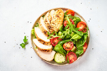 Green salad with grilled chicken meat at white table.