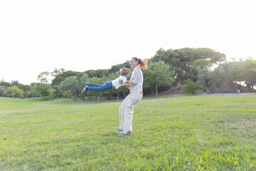 Naklejka premium Mother lifting and spinning her son in a park