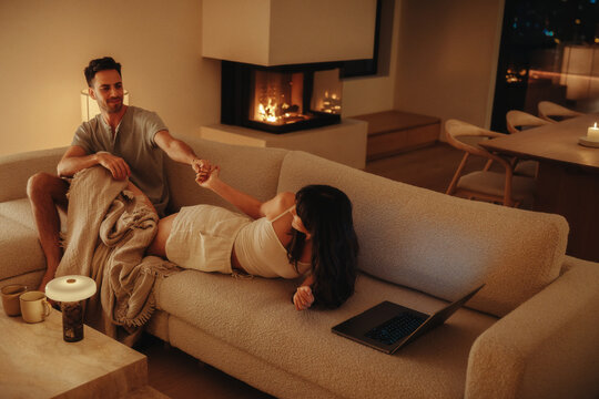 Woman pulling her partner by the hand on a living room couch at night