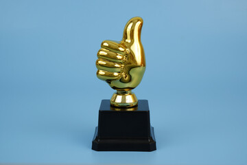 Golden champion thumbs up trophy cup on blue background. Good rating and feedback concept.