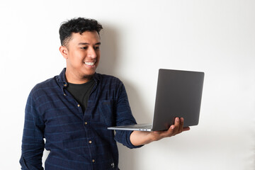 Adult Asian man looking to the camera while holding a laptop and showing happy expression