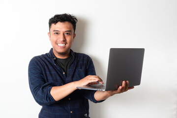 Adult Asian man looking to the camera while holding a laptop and showing happy expression