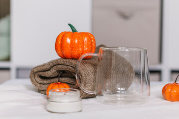 An empty glass mug, a candle in glass on the background of a folded sweater and orange pumpkins