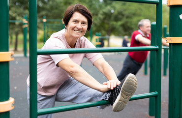 Obraz premium Positive elderly woman doing leg stretching on outdoor sports ground