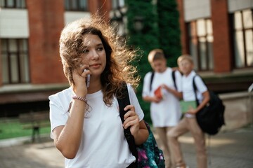 Girl is talking by phone. Kids are near the school together, pupils