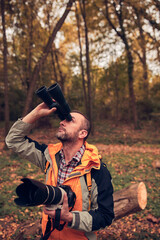 Man using binoculars and camera for bird and animal watching in nature.