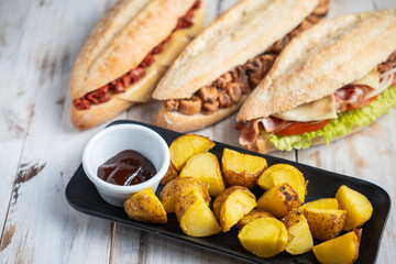 Three baguettes filled with different ingredients and a tray of potato wedges
