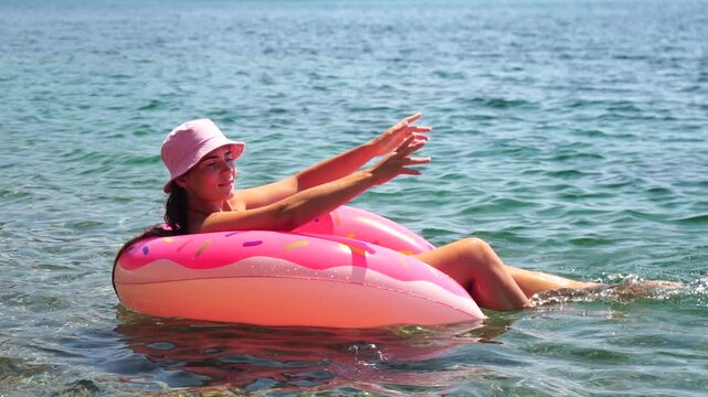 Woman Donut Float Beach - Smiling woman enjoys relaxing on pink donut float in clear blue water on beach.