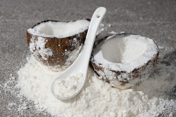 Coconut flour among coconut halves on gray stone background.