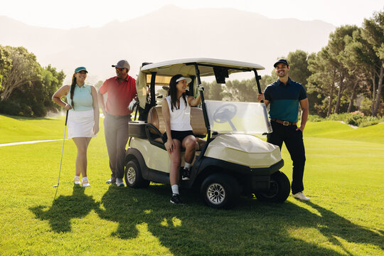 Group of golfing friends posing with golf cart on sunny fairway, enjoying vacation in stylish golf attire at scenic resort location