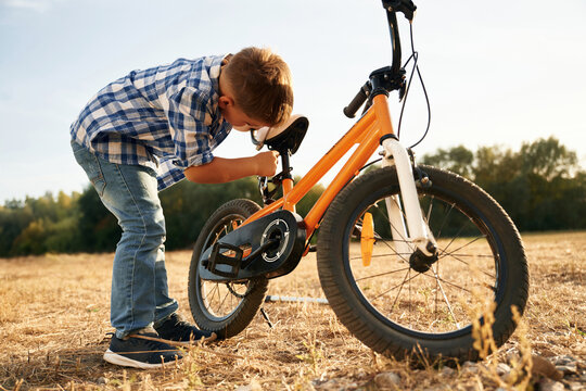 Repairing the bike, holding wrench. Cute boy is with his bicycle on the field