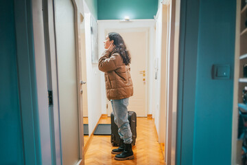 Side view of young Caucasian woman looks in the mirror in the hallway, and prepares to leave with a suitcase. Travel and business trip