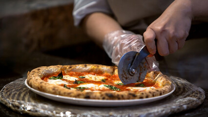 Chef slicing a freshly baked pizza on a metal tray. Traditional Italian cuisine