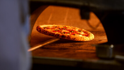 A pizza is baking on a stone in a traditional brick oven, surrounded by flames
