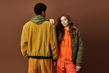 A fashionable couple showcases trendy autumn clothing in bright hues against a warm backdrop.