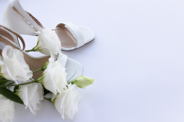 Bouquet of white flowers near white womans sandals. On a white background with a copy space. Selective focus.