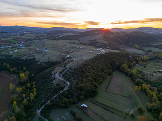Aerial View of Mountain Road in Village at Sunset in Autumn. Top View from Drone of Road in Woods. Beautiful Landscape with Roadway, Forest, Houses.