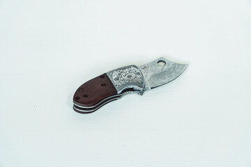 Mini folding knife with patterns on some parts of the blade isolated on a white background. Close-up view of a mini folding knife used for various outdoor or survival activities