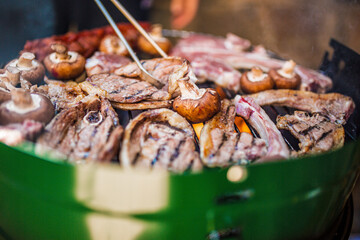 Meat and mushrooms grilling on a barbecue with tongs in view